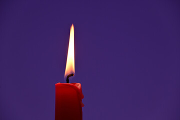 Burning red candle against a violet background
