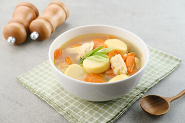 Clear soup with egg tofu, carrot and shrimp meatballs. Served in white bowl on grey background.
