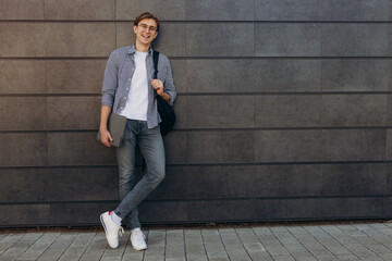 Happy student in glasses with laptop. Portrait of a young man with textbooks in his hands. Smiling boy with a backpack on dark wall. The concept of education. Copy space