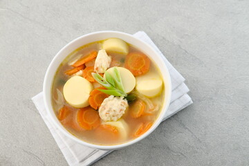 Clear soup with egg tofu, carrot and shrimp meatballs. Served in white bowl on grey background.
