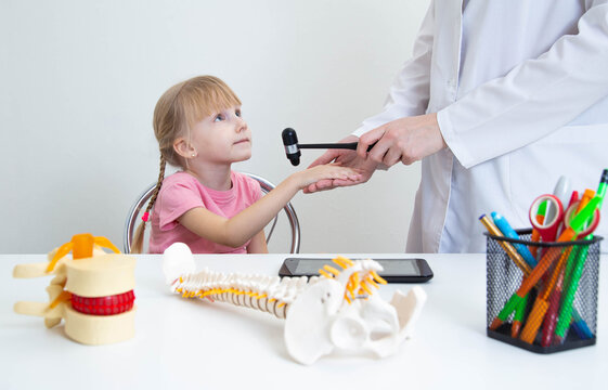 Doctor neuropathologist checks the reflex on the wrist joint with a neurological hammer in a beautiful 5-year-old girl. Caucasian baby