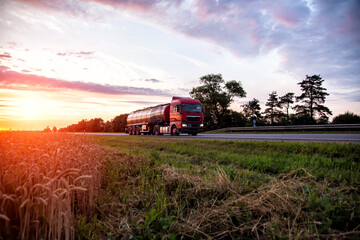 Fototapeta premium A modern truck with a semi-trailer tanker transports dangerous goods against the backdrop of a sunset in summer. Liquid cargo transportation. Copy space for text