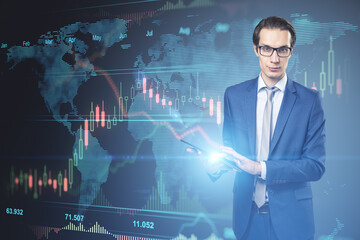 Attractive young european businessman with eyeglasses using tablet with glowing forex chart hologram on blurry background. Finance, trade and fintech concept. Double exposure.