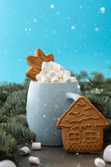Christmas drink with marshmallows in a mug with gingerbread cookies among fir branches and snow