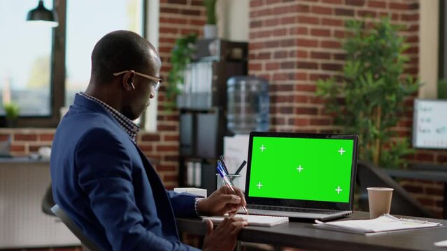 Office employee looking at laptop with greenscreen template, working in startup space. Sales consultant using isolated mockup background with chroma key display and blank copyspace.
