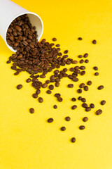 Takeaway white paper coffee cup on yellow background with pouring roasted beans out of it