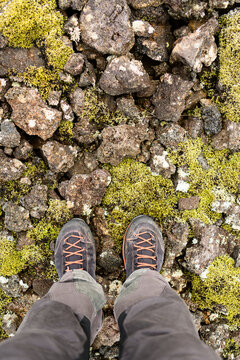 Legs in grey hinking trousers and black orange hiking boots on volcanic stones