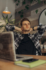 Male freelancer resting with hands behind head and looking away while having break during remote work in cafe 