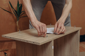 Unrecognizable man screwing bolt with metal hex key into wooden board while assembling new table and furniture at home 