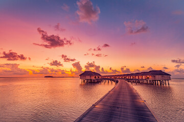 Sunset on Maldives island, luxury water villas resort and wooden pier pathway. Beautiful sky clouds...