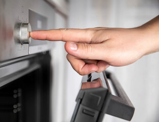 Modern oven with recessed function controls. Man's hand presses a recessed regulator, close-up.