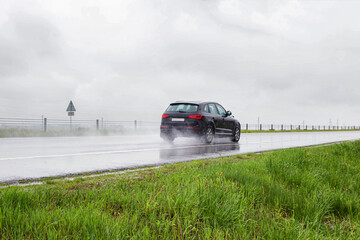 A modern black crossover car rides on a wet road in the rain in summer. Safety on a slippery road...