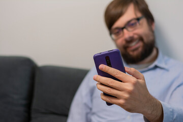 Close up selective focus on smartphone smiling man with beard and glasses in casual shirt waving hand taking selfie in living room at home. Healthy mental. Concept: using phone lifestyle 