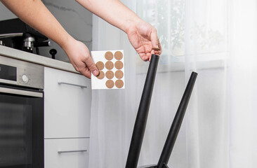 A man glues protective pads on the legs of a chair. Protection against floor scratches and noise