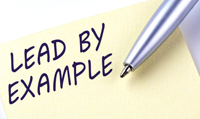 Sticky Note Message LEAD BY EXAMPLE with pen on the white background