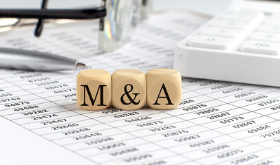 Fototapeta wooden cubes with the word M and A on a financial background with chart, calculator, pen and glasses, business concept. obraz