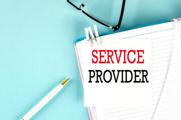 SERVICE PROVIDER text on a sticky on notebook with pen and glasses , blue background