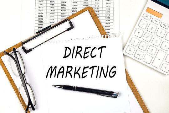 Text DIRECT MARKETING on the white paper on clipboard with chart and calculator