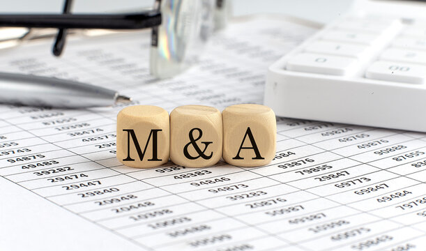 wooden cubes with the word M and A on a financial background with chart, calculator, pen and glasses, business concept.