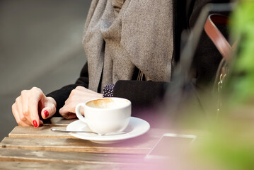 Elegant woman sitting at street caffe table drinking coffee