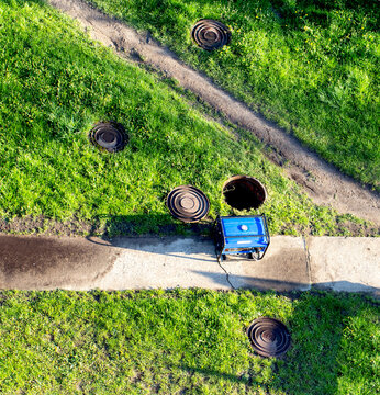 An open sewer well near which there is a gas generator on the grass. The concept of repair and maintenance of inspection and sewer wells. Accident in the water network, industry