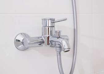 Modern silver chrome bathroom faucet with hot and cold water on a white wall. Close-up