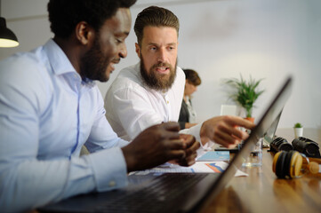 Diverse businessmen working on laptop together in office