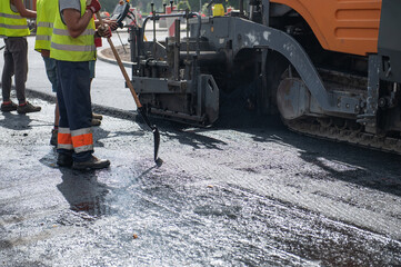 Workers operating asphalt paver machine during road construction and repairing works