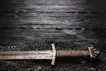 Ancient knight sword and chainmail on the wooden table flat lay background with copy space.