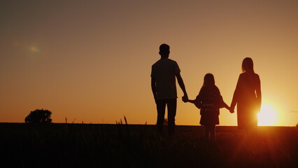 Fototapeta premium Young family with a child admiring the sunset in the field, holding hands