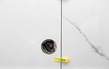 A hole in the wall with a tile for an outlet. Marble leveling system, close-up