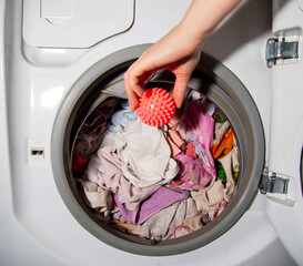 Woman throwing a red laundry ball into the washing machine, close-up. Hedgehog ball