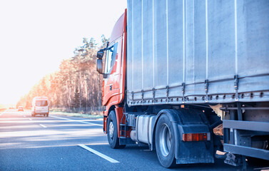 A truck with a trailer transports cargo on the road in summer in sunny weather. The concept of a...