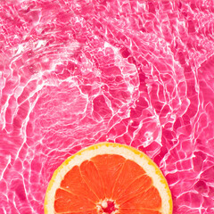 Fresh round grapefruit slice floating in a pool with a vivid pink water. Minimal summer fruit creative art. Aesthetic food concept. © Maja 