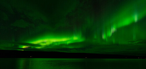 Northern lights over the plain lake with green reflections