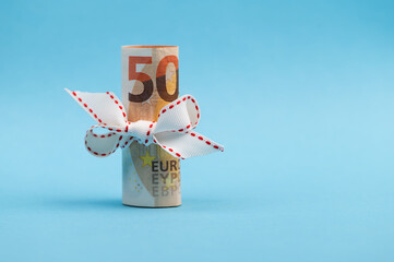 Roll of 50 Euro money with white ribbon isolated on light blue background