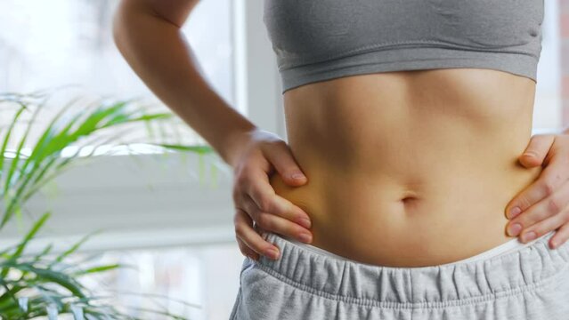 Woman compressing the skin on her stomach and sides checking for excess subcutaneous fat