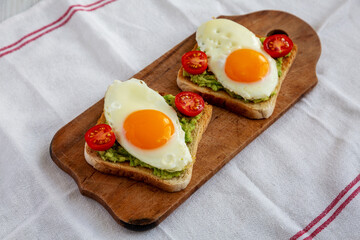 Homemade Healthy Egg, Avocado and Tomato Toast on a rustic wooden board, side view.