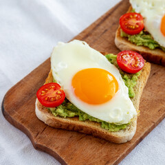 Homemade Healthy Egg, Avocado and Tomato Toast on a rustic wooden board, side view.