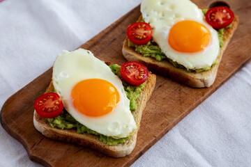 Homemade Healthy Egg, Avocado and Tomato Toast on a rustic wooden board, side view. Close-up.