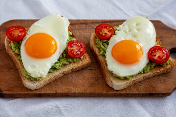 Homemade Healthy Egg, Avocado and Tomato Toast on a rustic wooden board, side view.