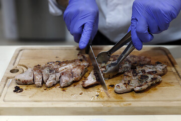 chef anónimo cortando con cuchillo y guantes carne de ternera en tabla de madera - obrazy, fototapety, plakaty