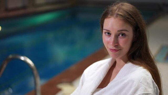 Young Happy Relaxed Woman Reading Book Sitting At Pool Indoors And Looking At Camera Smiling. Portrait Of Positive Confident Intelligent Tourist Posing In Spa Enjoying Vacations And Hobby