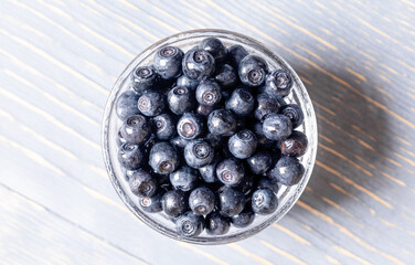 Wild forest blueberries in glass bowl close up on gray wooden table top view.