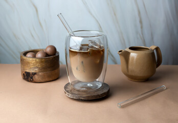 Pouring milk in coffee with ice cube on modern beige background. Iced latte coffee on modern still life.