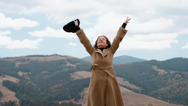 Girl stands against endless sky and admires nature and smiles. Woman feels freedom and raises hands up and breathes fresh mountain air. Female is filled with energy from nature. Calmness and serenity