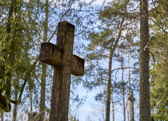 Ancient concrete cross in the cemetery covered by moss. Sunny day.