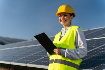 Portrait of smart lady engineer looking away while monitoring solar panels and smiling happy....