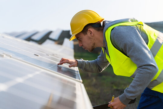 Close Up Of The Caucasian Worker In Signal Vest Touches Solar Panel And Checks For Damage Or Excessive Overheating