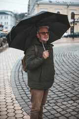 Mature man walks around the city in the rain with an umbrella, autumn stormy weather.